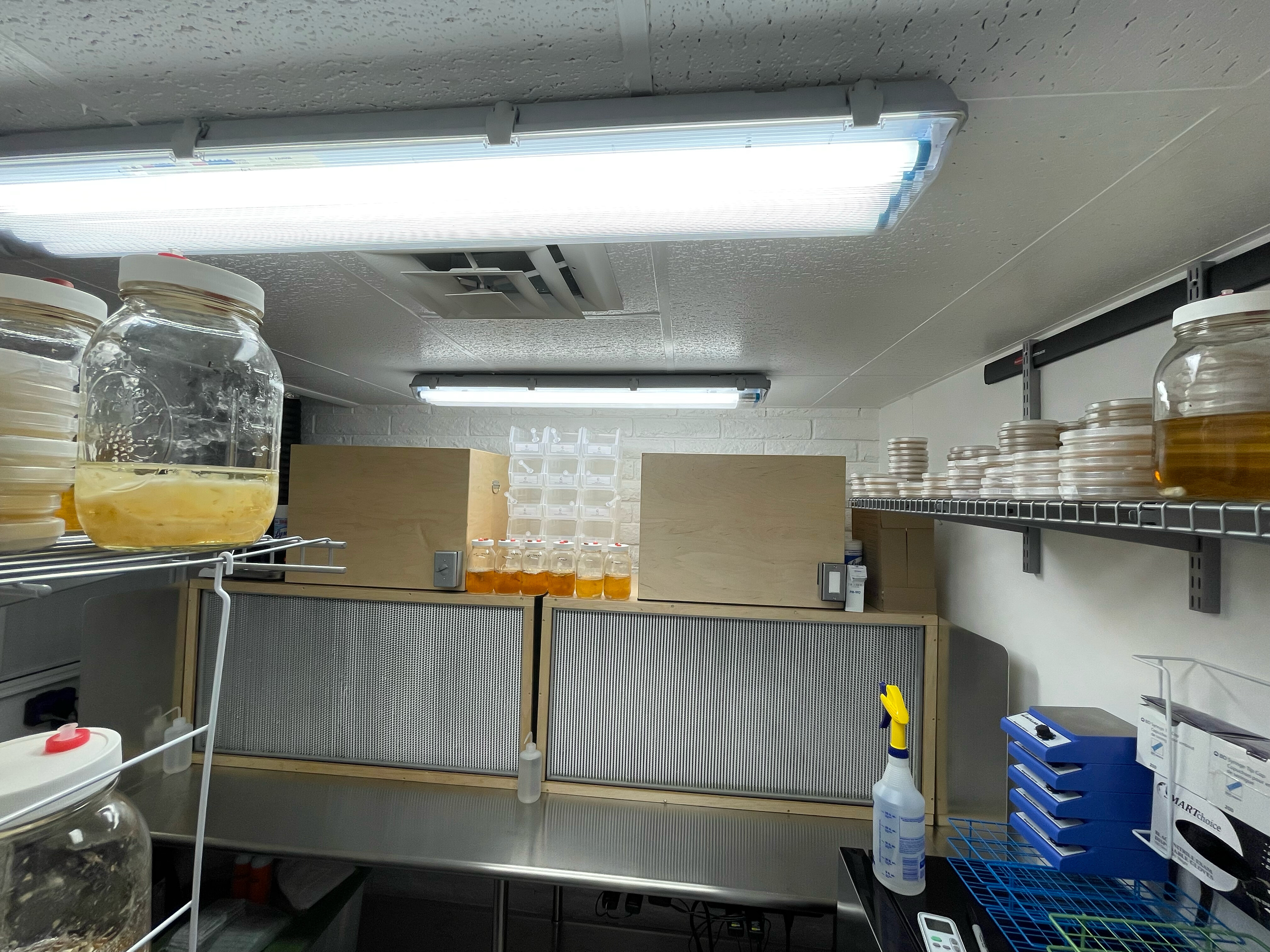 A clean room with benches, filter units, shelving and jars of liquid.